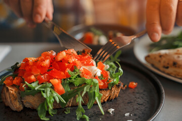 Close Up of Person Cutting Into Bruschetta With Knife and Fork