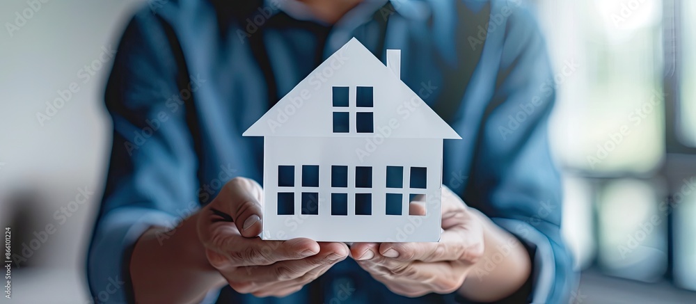 Aufkleber a man showcasing a paper house on a plain backdrop, utilizing it as a prop for educational and busin