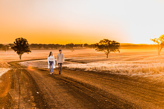 Teenage boy and girl walking together on rural dirt road at sunset