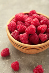 Raspberries in wooden bowl on grey concrete background