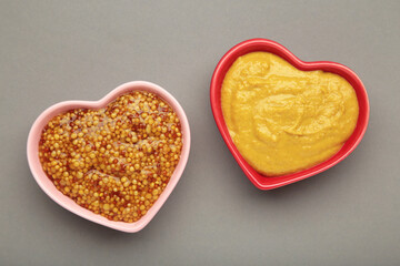 Dijon mustard with french mustard on heart shaped bowl on grey background.