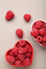 Fresh ripe garden raspberry in heart shaped bowl on grey background. Top view with copy space