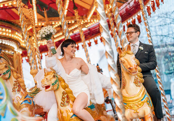 Bride And Groom Ride Carousel Horses During Wedding Day Celebration