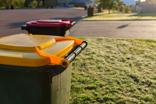 Recycling bin siting on suburban roadside in morning light with rubbish wheelie bin