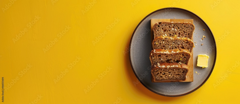 Poster top view of wholegrain bread on a cutting board with butter on a plate, set against a yellow backgro