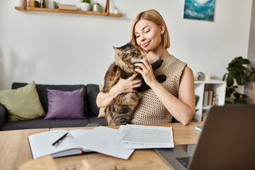 An attractive woman with short hair sits at a table, holding her cat close to her.