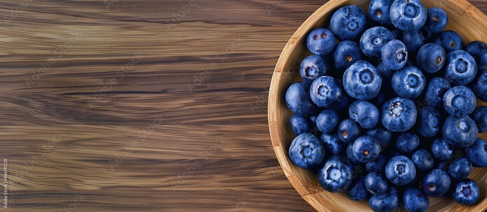 Poster top view of fresh blueberries on a wooden plate with a wooden table background, with copy space imag
