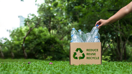 Reduce, reuse and recycle concept. A hand places a plastic water bottle into a cardboard box. An...