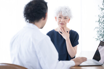 医師に体の不調を訴える高齢の患者と診察する医師　喉の痛みなど
