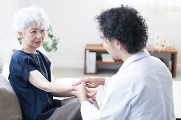 自宅へ訪問診療にくるドクターと高齢者の患者のイメージ　脈をとる