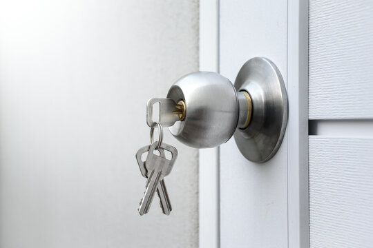 Keys and silver knob on a white wooden door against against the gray concrete background for forgot to close the door or lost the key and safety with security concept.