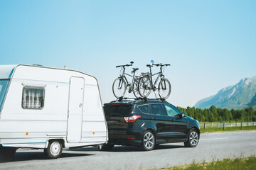 Car with bicycles mounted on top towing a caravan on a sunny highway against a scenic mountain...