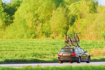 Fototapeta premium Car with roof-mounted bikes driving through lush green fields and forests