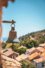Fototapeta premium Church bell in a tower against a clear blue sky, with a softly blurred background of a quaint village or town.