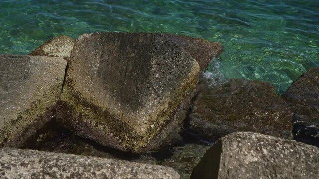 Concrete blocks in clear turquoise seawater with green algae growing on the surfaces in an outdoor seaside setting.