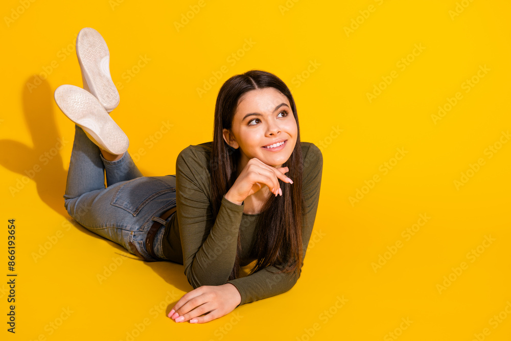 Sticker Full body photo of attractive teen woman lying floor admire look empty space dressed khaki clothes isolated on yellow color background