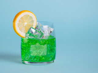 Summer drink in a glass on a blue background, majito with ice and a slice of lemon