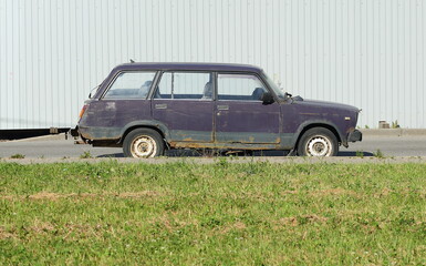 An old purple Soviet car stands between a fence and a lawn, Soyuz Avenue, St. Petersburg, Russia,...