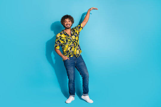 Full size photo of funky man dressed print shirt jeans palm demonstrate large height empty space isolated on blue color background