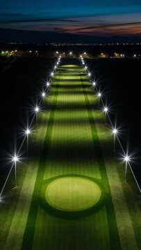 A stunning aerial view of a par 3 golf fairway illuminated by bright streetlights on either side, late at night