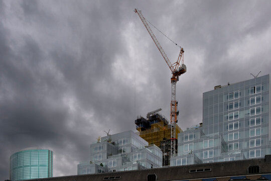 Construction site featuring a large crane and modern glass buildings under a dramatic sky with dark clouds, symbolizing progress and development amidst changing weather.