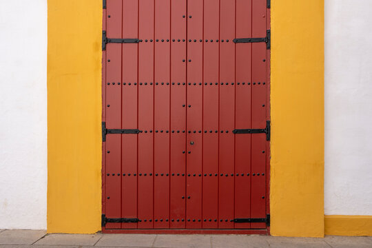 in Seville in Spainstriking red door with a yellow border set against a stark white wall, showcasing a vibrant and contrasting architectural detail.