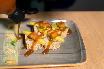 Chef in the restaurant kitchen decorating delicious rolls with sesame sauce from a bottle, close-up. Concept of food