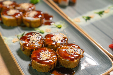 Close-up of delicious hot Banzai sushi with rice, cream cheese, salmon, panko, sesame seeds, teriyaki sauce on a beautiful rectangular dish. Concept of traditional Japanese food