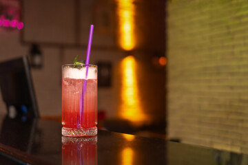 Close-up of a strawberry alcoholic cocktail in a glass with foam decorated with a sprig of rosemary and a straw stands on the bar counter in a beautiful modern bar, copy space.