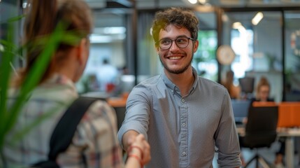 A young manager with a cheerful smile extends a handshake to a new employee in a modern office setting