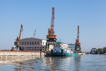 Fototapeta premium Ruse port view with portal cranes at the embankment and a push boat