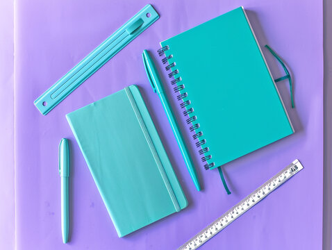A collection of three turquoise stationery items, including a notebook, pen, and ruler, arranged in a triangular formation on a lavender backdrop with some copy space
