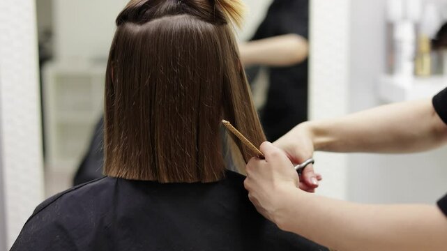 Unrecognisable hairdresser cutting female client hair with professional barber scissors and comb and making stylish haircut short bob hairstyle in beauty salon. Hair care, hair salon and hairstyling.