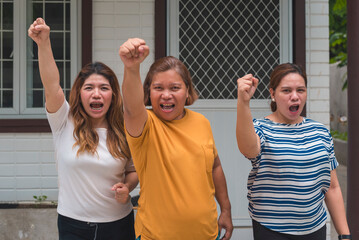 Three asian women raising their fists in protest after being charged unfair rental increases for...