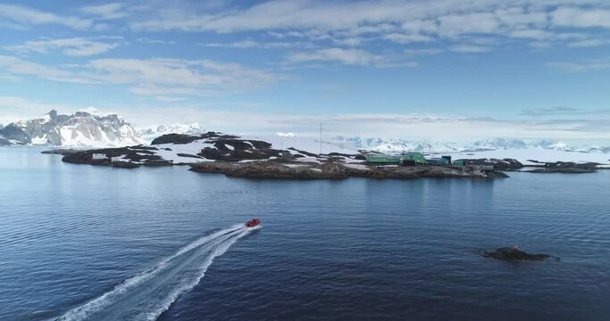 People on motorboat sailing polar ocean coastline in Antarctica. Science research Vernadsky base station on rocky island bay. Expedition, explore. Travel, tourism on South Pole. Aerial drone shot