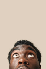 Obraz premium African American man looking up with thoughtful expression, closeup portrait against light beige background