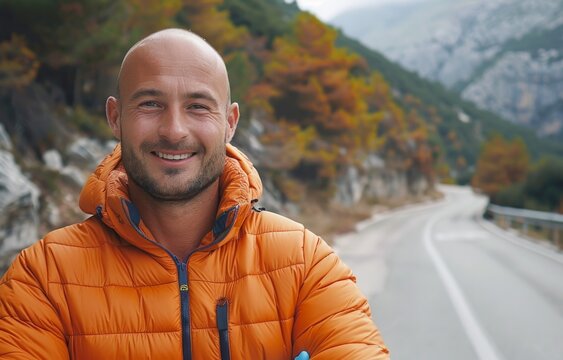 Smiling bald man in orange jacket enjoying a scenic mountain road journey in autumn