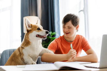 Happy teenager, boy with down syndrome doing homework with dog