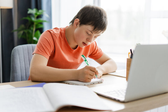 Young student with down syndrome is studying at home using laptop, sitting at home