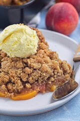 Delicious Peach Crisp or cobbler on plate with scoop of vanilla ice cream, vertical, closeup