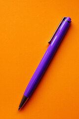A purple pen positioned in the bottom left corner of a solid orange background, perfect for writing and drawing.