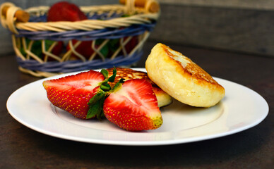 Cottage cheese pancakes, syrniki, curd fritters , decorated with fresh strawberry, served on a white plate on dark background. Homemade breakfast.