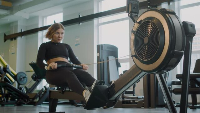 Young Caucasian female athlete using rowing machine while training at gym