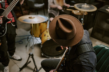 High angle view of unrecognizable man in hat sitting on chair and playing guitar during rehearsal or performance with band