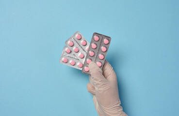 Female hand holding round pills in a blister pack on a blue background, top view