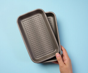 Hand holds black disposable polystyrene foam rectangular plate for packaging vegetables and meat