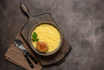 Mashed potatoes with cutlet in a bowl on a wooden board, dark rustic background. Top view, flat lay