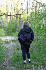 girl walking in the woods back view. young woman in spring forest. girl with a backpack, tourist. enjoying spring weather. Rest, relaxation, lifestyle, walk in the fresh air. hiking in nature