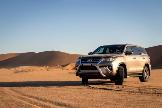 A gray Toyota Fortuner in the middle of the Namib Desert against a bright sky