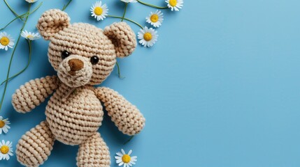 Handmade amigurumi teddy bear with daisies on blue background baby theme top view with space for text